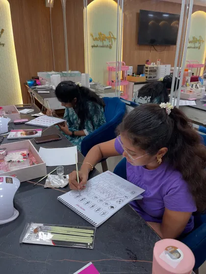 A student practices drawing different nail shapes and art designs in her workbook. This foundational skill is crucial before working on actual nails.