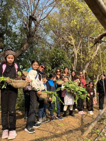 A line of children and adults holding baskets overflowing with freshly picked leafy greens.