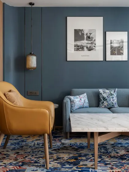A composition of contrasts defines this suite's living area. Moody blue walls anchor the setting, a sleek marble coffee table introduces elegance, while a mustard armchair injects vibrancy and warmth.