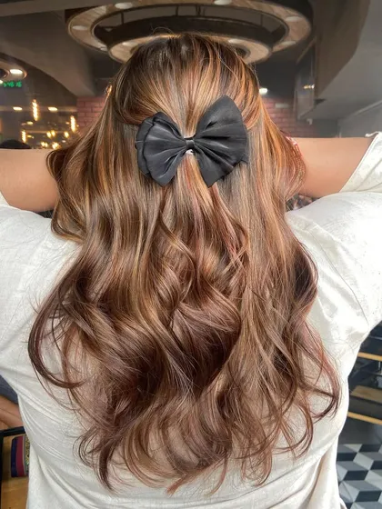 A cute bow adds a touch of style to this honey and caramel balayage, showcasing its versatility for different looks.