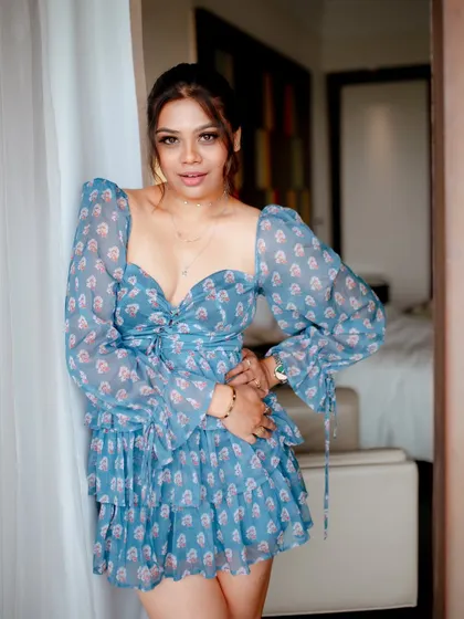 A smiling portrait of a model in a blue floral dress. The indoor setting and her happy expression create a bright and cheerful lifestyle image.