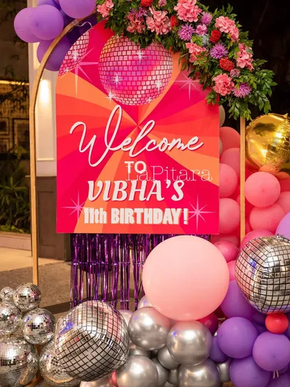 A vibrant welcome sign for Vibha's 11th birthday, decorated with disco balls and a pink and purple balloon arrangement.