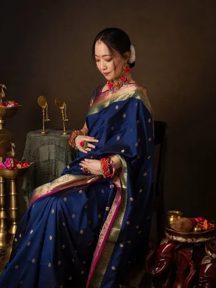 A moment of quiet contemplation. Seated gracefully, she cradles her bump, wrapped in the rich blue and gold of the saree. The lighting creates a painterly, classic feel.