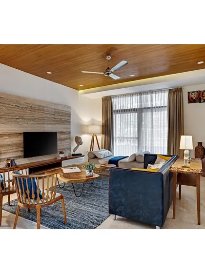 The formal living room in Nataraj House, where a natural Travertine stone TV wall, a live-edge coffee table, and a deep blue sofa create a sophisticated yet comfortable space.