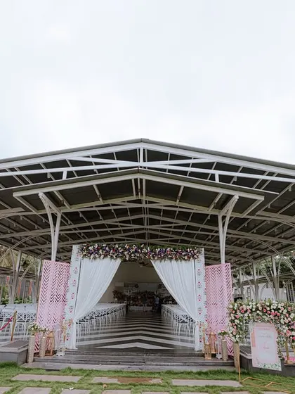 The entrance to a modern reception venue, elegantly decorated with soft pink and white drapes and floral arrangements. The checkered floor and red rope barriers add a touch of classic glamour.