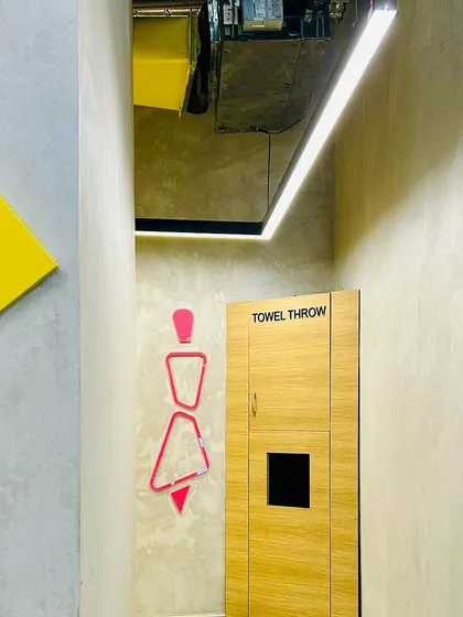 The design extends to the smallest details, like the stylized restroom signage and a dedicated towel drop. These thoughtful touches enhance the user experience and maintain the gym's clean, modern aesthetic.