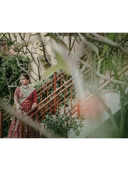 An artistic shot of the bride on a staircase, framed by green foliage, creating a sense of looking in on a private, serene moment.
