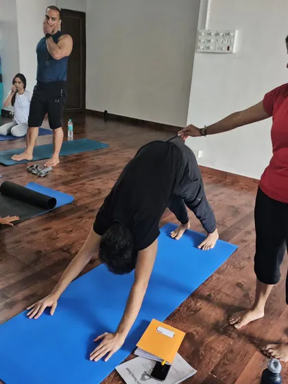 A teacher assists a student in Downward-Facing Dog, ensuring their hands are grounded and their spine is long.