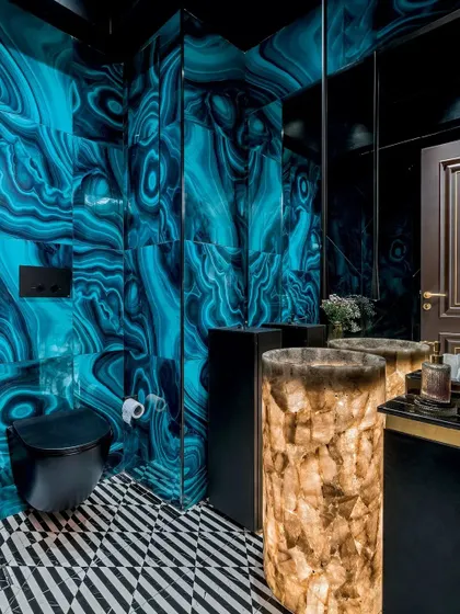 A powder room that makes a bold statement. The walls are clad in a vibrant blue malachite-patterned tile, contrasted by a striking illuminated quartz pedestal sink. The geometric black and white flooring adds another layer of graphic drama.