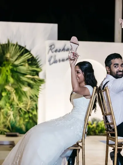 Fun and games at the reception. The couple plays the classic shoe game against a simple, modern backdrop with lush green foliage, showing that the decor can be a perfect setting for candid moments.