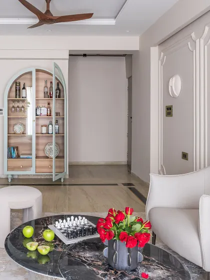 A beautiful shot of the 'Modern Muse' living room, featuring a custom-designed arched bar cabinet in a subtle mint green, a black marble coffee table, and elegant white armchairs.