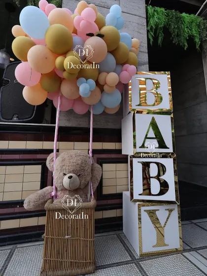 A large teddy bear in a hot air balloon basket next to "BABY" blocks, a perfect photo op.