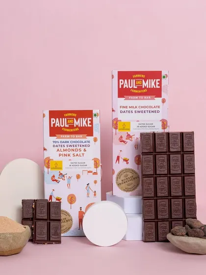 Two varieties of date-sweetened chocolate bars, styled with their raw ingredients for a clean and informative product shot.