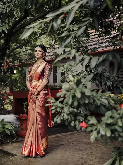A full-length bridal portrait set in a lush, green environment. The framing through the leaves adds depth, creating a sense of the bride being in her own peaceful, natural world.