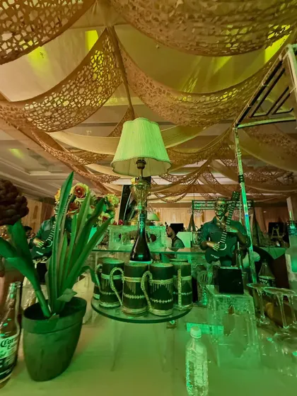 A rustic-themed decor setup with a green-lit lamp, wooden mugs, and musician figurines under a camouflage-netted ceiling.