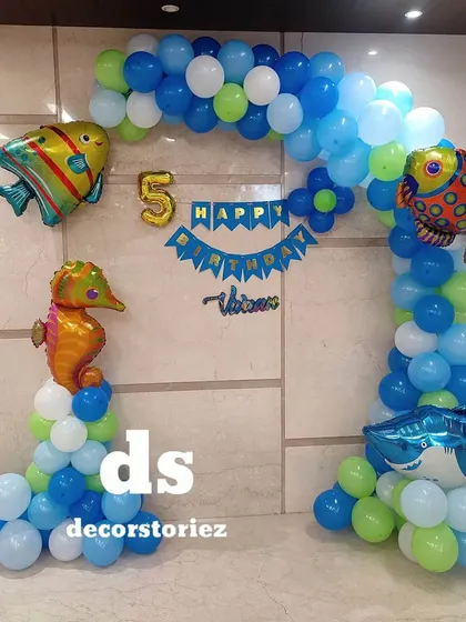 An underwater adventure with this ocean theme birthday decoration. The blue and green balloon arch features fun sea creature foils like fish, a seahorse, and a shark.