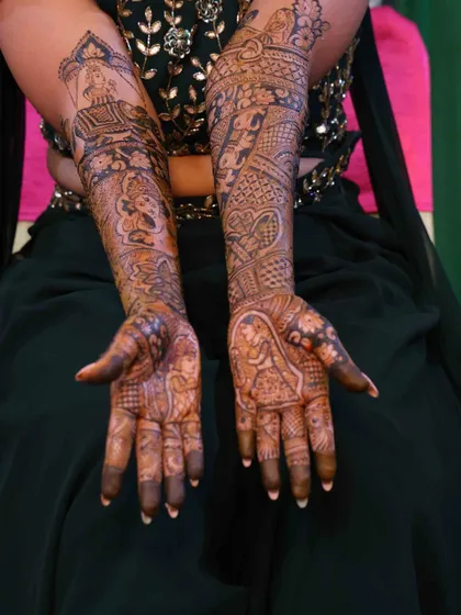 A full view of a bride's intricate arm mehndi. The design is filled with traditional elements, including portraits and detailed filler patterns for a rich, heavy bridal look.