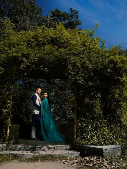 A wide shot of a couple standing under a natural archway of lush green foliage. This image shows how I use natural frames within the landscape to create depth and focus in a pre-wedding photograph.