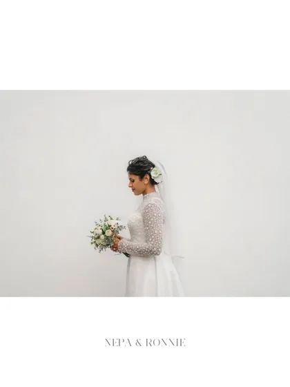 A minimalist and elegant bridal portrait against a clean white wall. The simplicity of the background allows the bride's grace and beauty to be the sole focus.