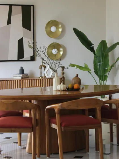 A close-up of the dining area, where warm wood furniture with red upholstery is set against a backdrop of abstract art and brass wall sconces. The space feels both vibrant and grounded.