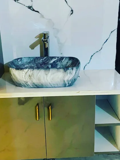 A close-up of a stylish vanity setup. The design includes a beautiful marble-patterned vessel sink, a sleek chrome faucet, and a simple cabinet for storage.