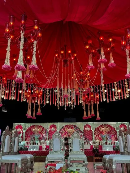 This mandap features a dramatic red draped ceiling from which hang floral-adorned chandeliers and strings of jasmine, creating a rich and romantic atmosphere.