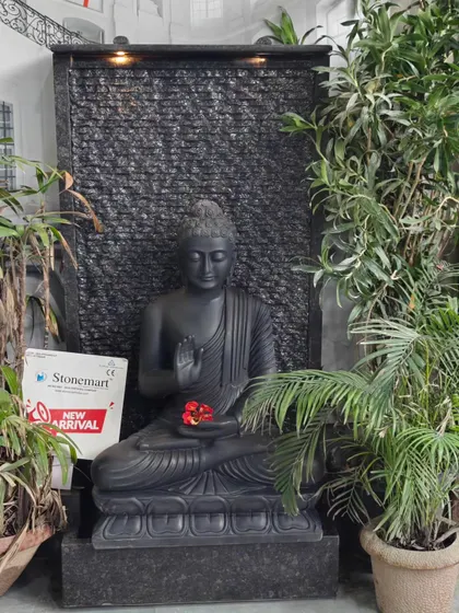 The black marble Buddha fountain surrounded by lush greenery. The dark stone of the fountain contrasts beautifully with the vibrant plants, making it a natural fit for a garden.