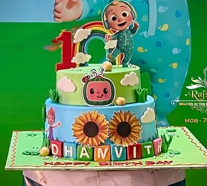 Themed cakes are a crucial part of our party planning. This two-tier Cocomelon cake is intricately designed with characters, a rainbow, and personalized name blocks, serving as a delicious centerpiece for the celebration.