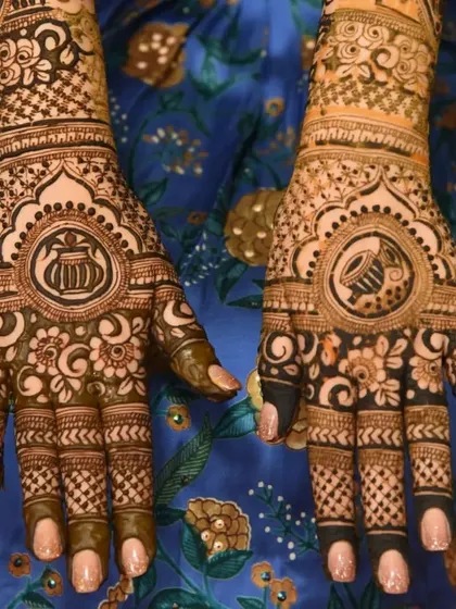 A beautiful bridal design with symbolic motifs. One palm features a 'kalash' (pot), while the other has a 'dholak' (drum), both central to wedding rituals. The surrounding floral patterns are intricate and dense.