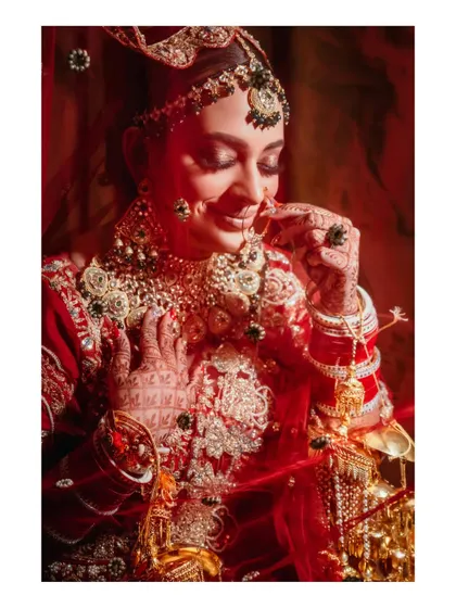 A beautiful portrait of the bride adjusting her nath (nose ring). The red lighting and her gentle expression create a soft and romantic mood.
