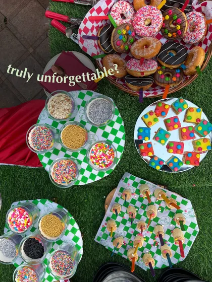 A colorful and fun dessert spread for a kids' party, featuring a donut basket, sprinkle-covered cookies, and marshmallow pops. This is a sweet-lover's dream come true.