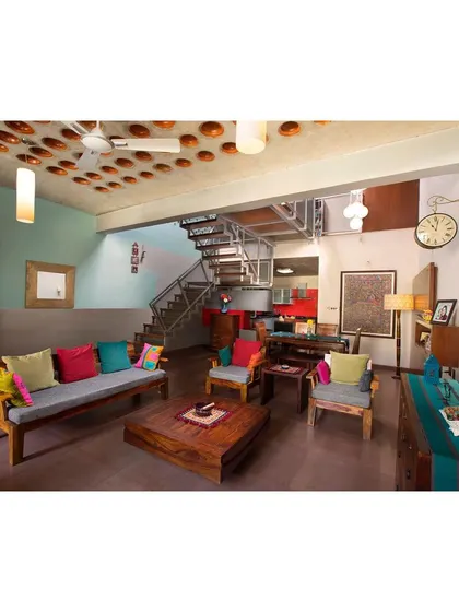 Another view of the Interlocking House living area, highlighting the solid teak wood furniture. The simple, strong forms of the sofa and chairs provide a durable and timeless foundation for the room's eclectic decor.