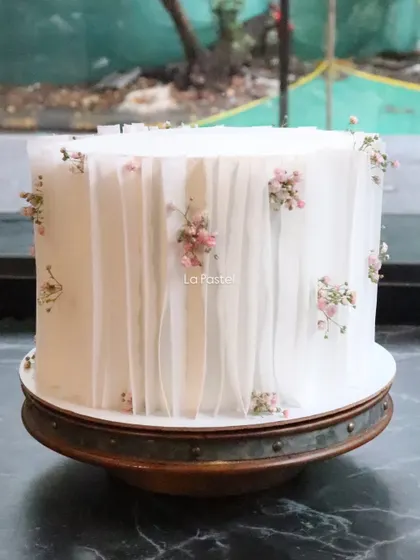 A beautiful cake decorated with a delicate wafer paper curtain effect and tiny pink flowers.
