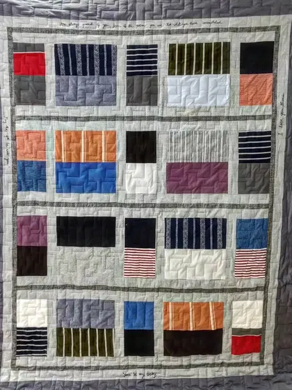 A full view of a modern memory quilt made from T-shirts, with embroidered messages in the border.