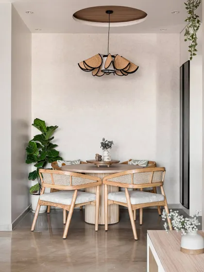 This cozy dining nook features a round wooden table and chairs with woven rattan backs, creating a warm and inviting atmosphere. The statement pendant light adds a touch of modern, sculptural art to the space.