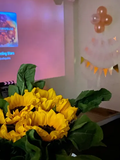 A beautiful bouquet of sunflowers adds a touch of brightness to the room, contrasting with the movie playing on the projector in the background.