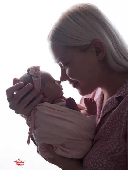 A mother and her newborn baby share a gentle moment, nose to nose. The soft backlighting creates a beautiful silhouette effect, emphasizing the tender connection.