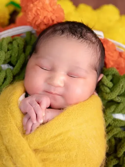 A close-up from our Diwali series. A baby wrapped in bright yellow rests in a basket adorned with festive marigold flowers, radiating warmth and light.