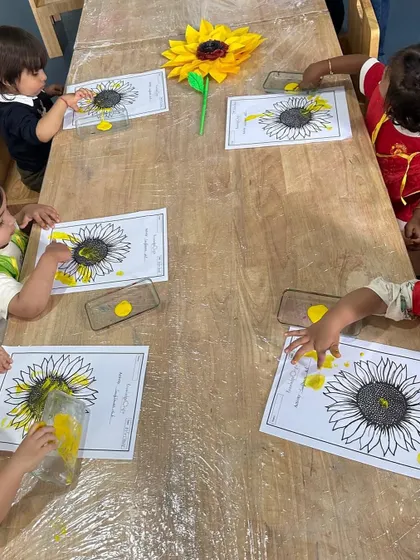 Our Independent Toddlers work at a child-sized table, finger-painting sunflowers. This activity strengthens fine motor skills and introduces them to nature themes.