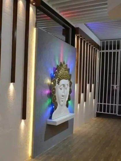This wall feature uses a combination of concrete-finish panels, wood battens, and strategic lighting to highlight a Buddha sculpture, creating a tranquil focal point.