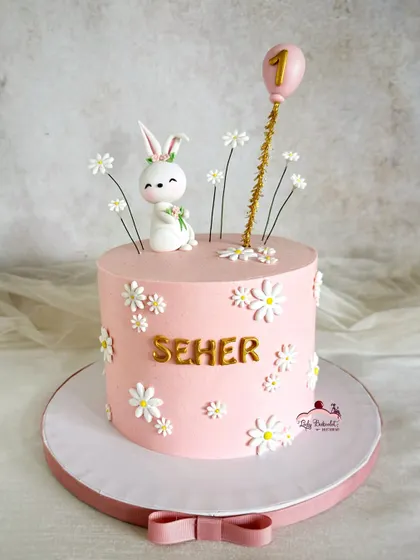 A hoppy first birthday cake! This design features a cute bunny, a field of daisies, and a pink balloon topper.