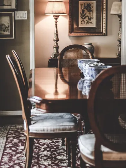 A classic dining setting featuring a polished solid wood table and traditional chairs with cane-back detailing. The warm lighting and rich wood tones create a timeless and inviting atmosphere.