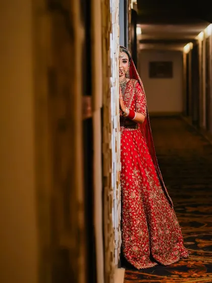 A playful yet elegant shot of the bride peeking from behind a wall in a hotel corridor. This image combines traditional attire with a modern, candid feel.