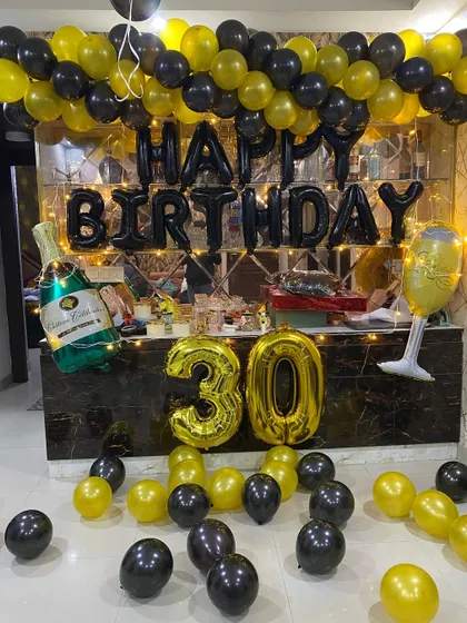 A 30th birthday party setup with black and yellow balloons, number balloons, and champagne-themed foil balloons.