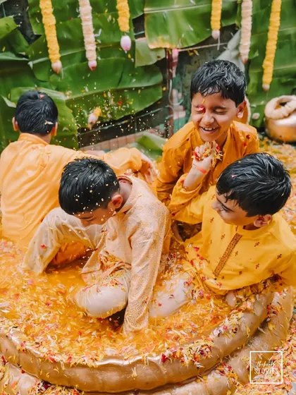 A heartwarming and fun shot of young boys playing in a tub filled with flowers and turmeric water during the Haldi ceremony. It captures the joy that permeates the entire family.