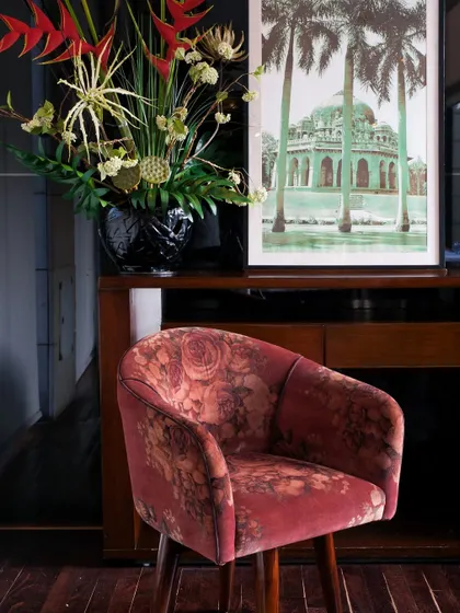 A detail shot of our decor, featuring a plush, floral-patterned chair, elegant floral arrangements, and artwork that reflects our modern Indian ethos.