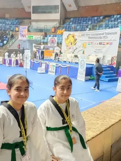 Two of our students, dressed in their taekwondo uniforms with green belts, pose for a photo at the international championship venue. Their smiles reflect their pride and excitement.