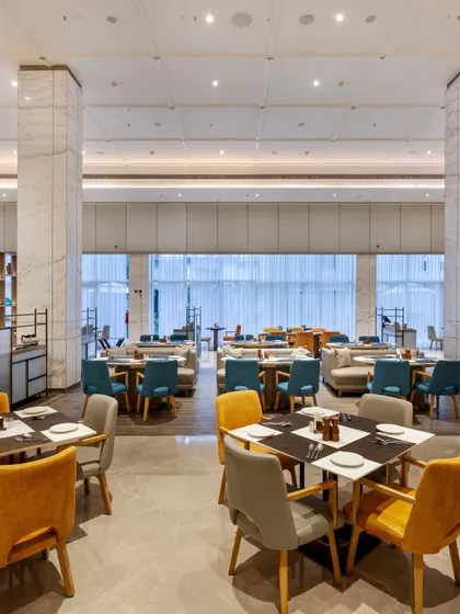 A view across the dining area, showing the spacious layout and clean, modern aesthetic. Marble-clad pillars and floor-to-ceiling windows create a bright and airy atmosphere for guests.
