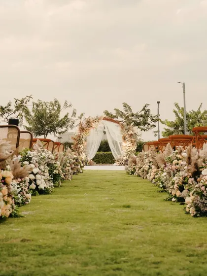 The aisle for the vow exchange, lined with arrangements of dried grasses and fresh flowers, leading to a romantic, draped arch.