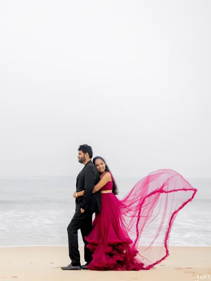 A beautiful shot of a couple on the beach, with the bride's vibrant red gown flowing in the sea breeze. This image combines elegant posing with the natural beauty of the coastline for a classic pre-wedding portrait.